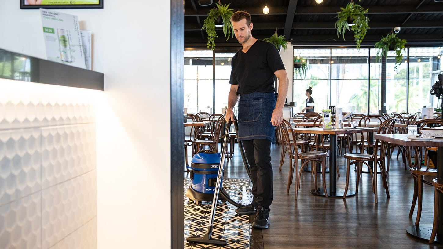 Manager of a restaurant using a Pacvac Hydropro 21 commercial wet and dry vacuum to clean the tiled area between the bar and the restaurant seating.