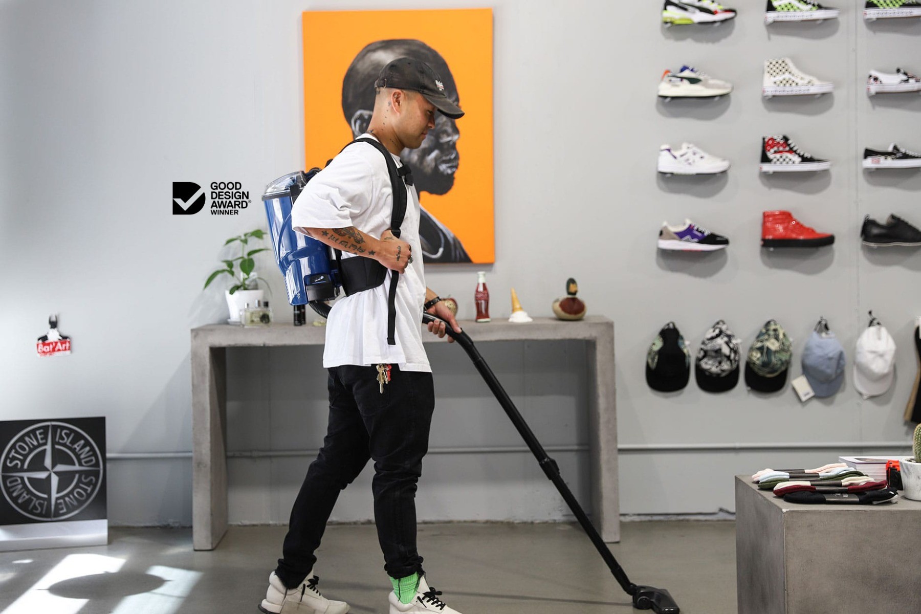 Man vacuuming the floor of Cabinet Noir, a designer streetwear clothing store, with a Velo battery powered vacuum, between clothing racks.